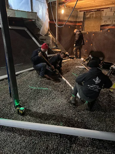 Crew installing interior waterproofing drainage and gravel base along an open basement slab