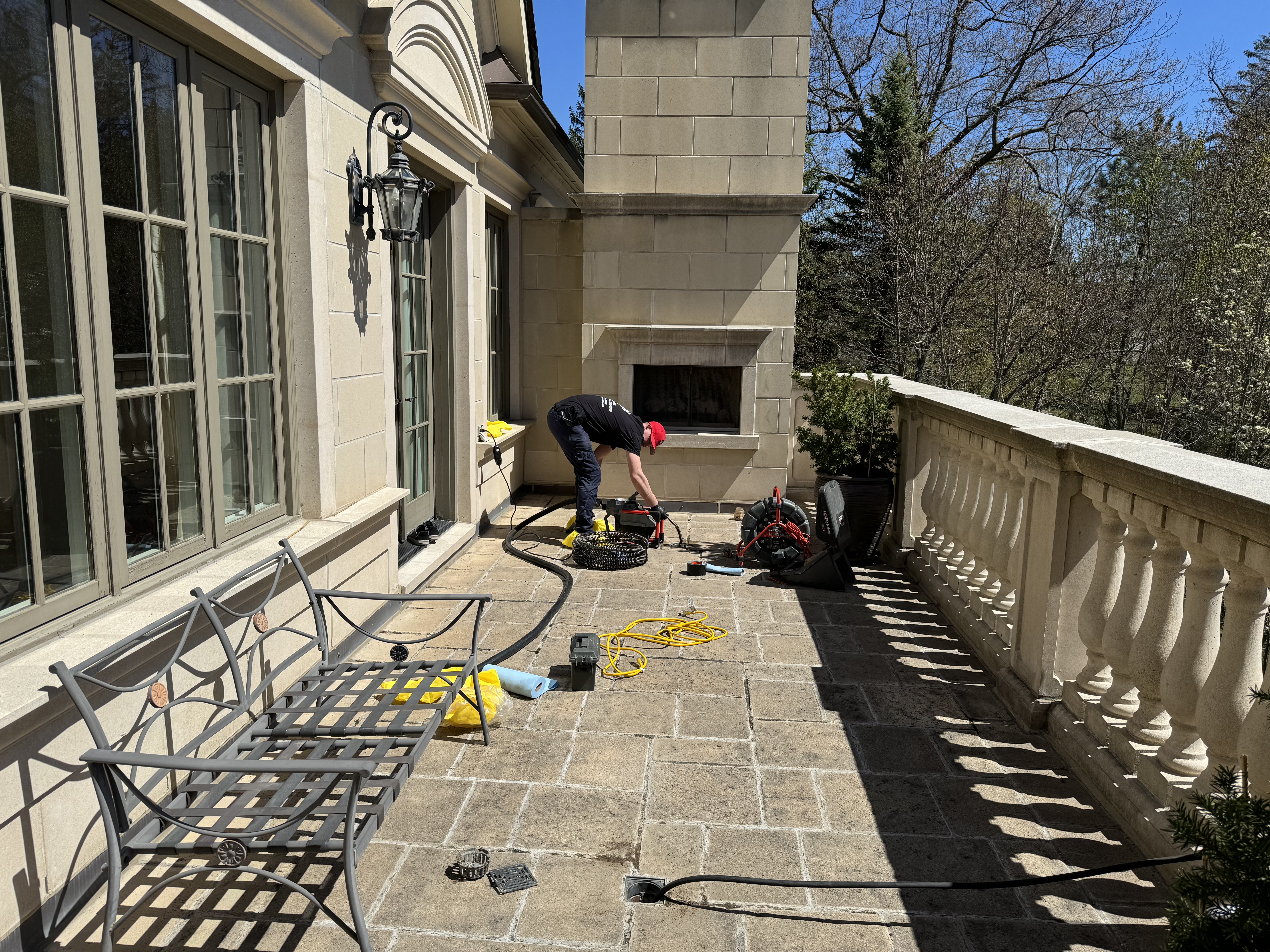 Technician setting up drain service equipment on a stone terrace outside a home